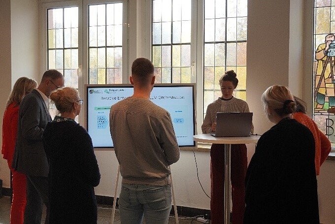 Mitarbeitende stehen vor einem Präsentationsbildschirm.