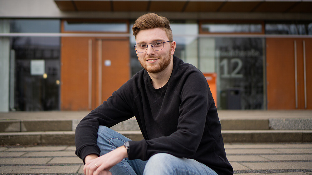 Johannes Krutz sitzt vor der Mensa auf den Treppenabsatz.