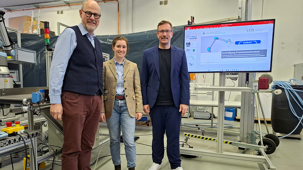 Drei Personen stehen im Labor, daneben ein Bildschirm, auf dem eine Grafik zu sehen ist.