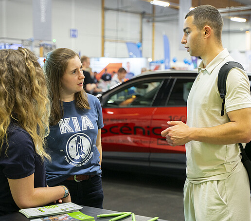 Zwei Mitarbeiterinnen im Gespräch am KIA-Stand mit einem Besucher.