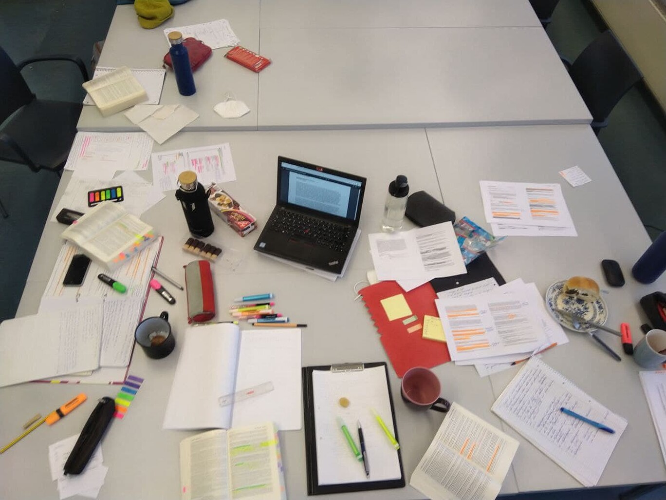 Blick von oben auf einen voll gefülltem Tisch mit Büchern, Zetteln, Stiften, ein Notebook usw.