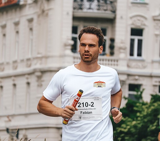 Ein Läufer hält den Staffelstab und läuft auf dem Campus.