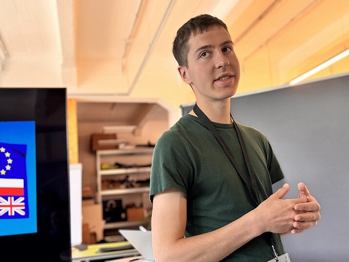 Ein junger Mann im grünen T-Shirt mit Schlüsselband steht in einem Raum 