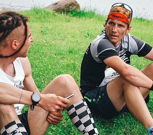 Zwei Läufer sitzen auf der Wiese und unterhalten sich nach dem Lauf.