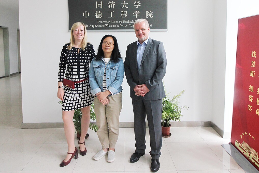 Zwei weibliche und eine männliche Person in einem Raum mit verschiedenen Schildern mit chinesischer Schrift.