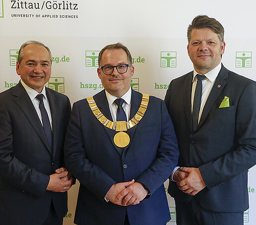 Vor einer Pressewand stehen Herr Ursu, Prof. Kratzsch und Herr Zenker nebeneinander und schauen in die Kamera.