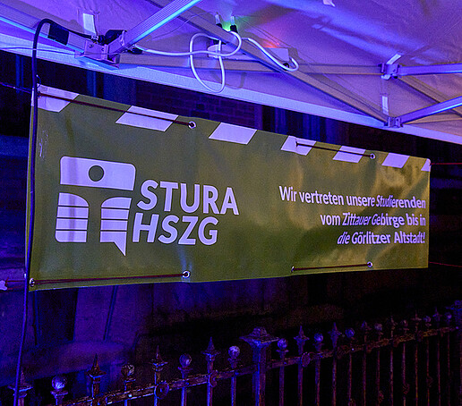 Ein grün-weißes StuRa-Banner hängt an einem Pavillion.