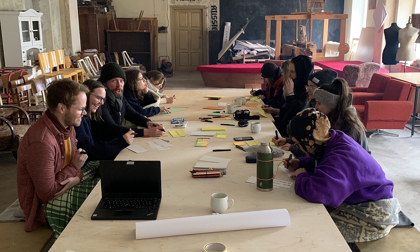 Eine Gruppe Studierender an einem Tisch mit Notebook, Zetteln, Stiften und Tassen..