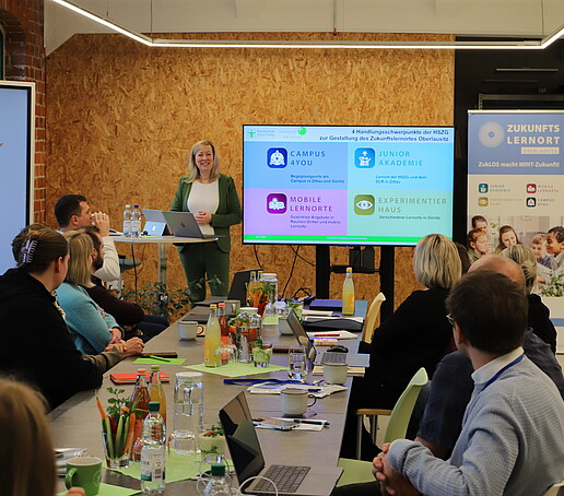 Workshopteilnehmende sitzen im Celsiuz am Tisch und die Prorektorin richtet von einem Stehtisch aus Worte an sie.