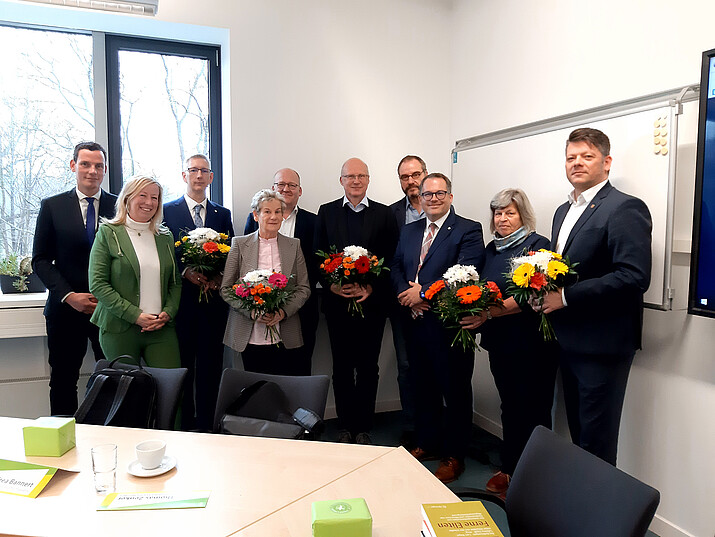 Der Hochschulrat und das Rektorat stehen im Seminarraum als Gruppe zusammen und lächeln in die Kamera.