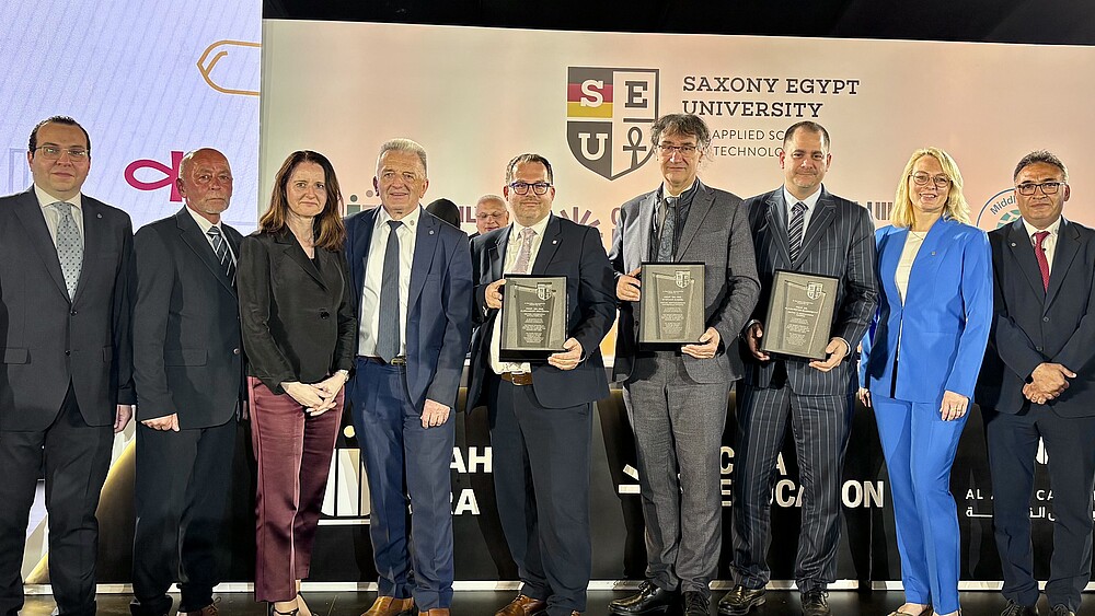 Der Ministerpräsident und Vertretende der sächsischen Hochschullandschaft zeigen auf dem Podium ihre unterzeichneten Vereinbarungen in die Kamera.
