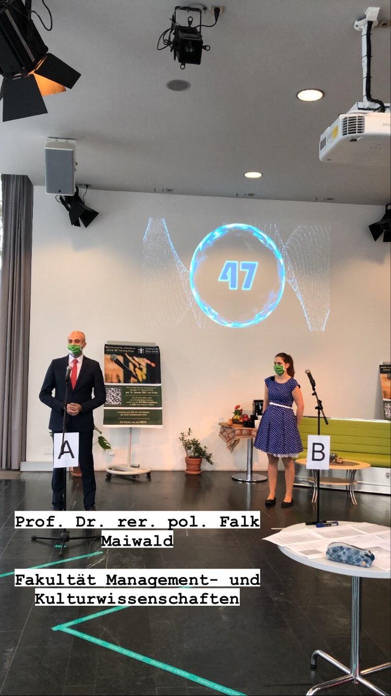 Bild des Dozenten und Moderatorin auf der Bühne.