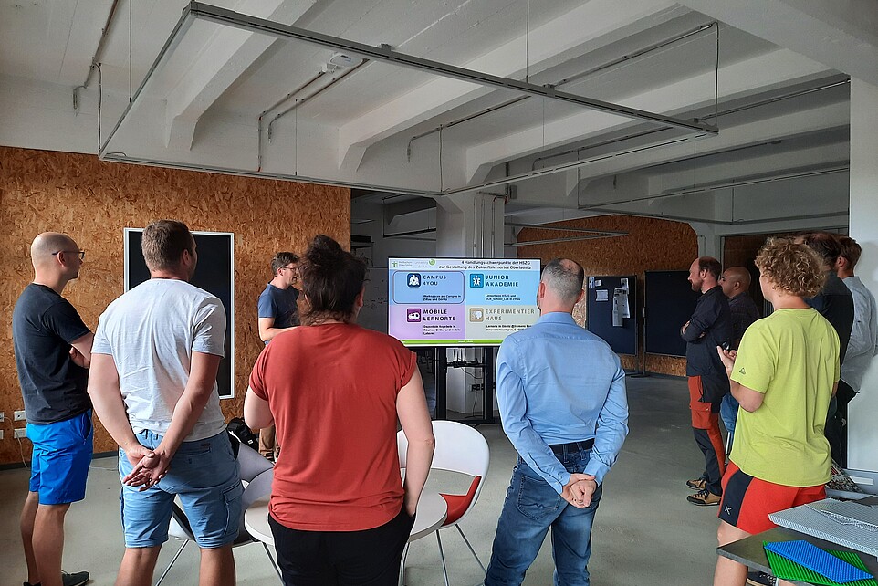 Interessierte schauen im Celsiuz auf einen Bildschirm und hören Egmont Schreiter zu.