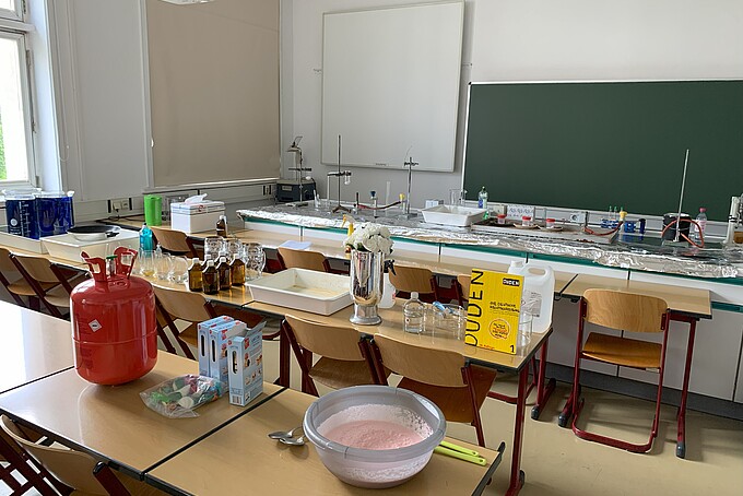 Experimentieranordnungen stehen auf Tischen im Seminarraum. Das Podium vor der Tafel ist mit Alufolie bedeckt, darauf ist eine Experimentieranordnung aufgebaut.