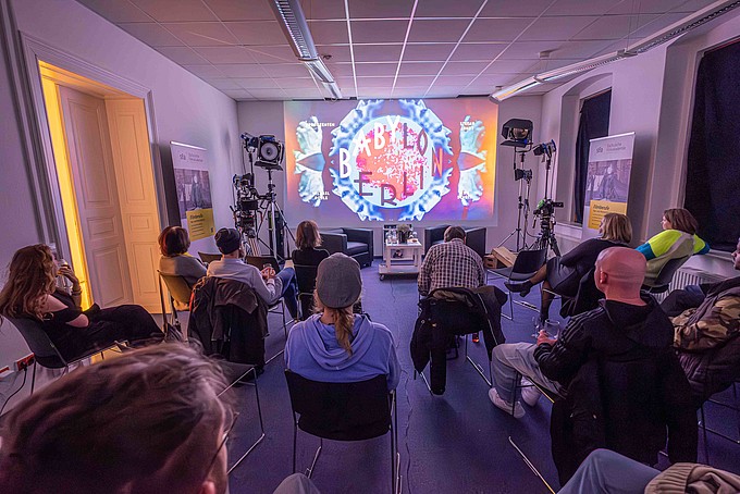 Teilnehmende eines Werkstattgespräches schauen sich in einem Seminarraum die Leinwandübertragung eines Films an.