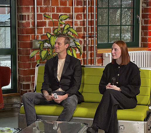 Zwei Interviewgäste der Morningshow sitzen im TV-Studio auf einem grünen Sofa.