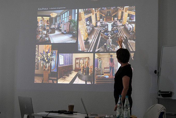 Die Dozentin schaut im abgedunkelten Seminarraum auf eine Beamerprojektion, auf der verschiedene Filmkulissen zu sehen sind.