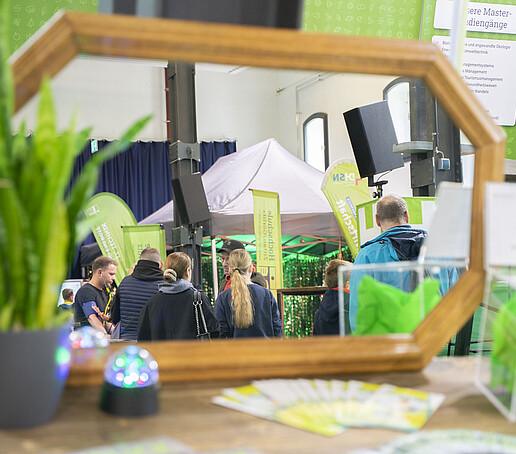 In einem Spiegel sieht man Besuchende, die sich am gegenüberliegenden Tisch beraten lassen. Eine Grünpflanze steht links vor dem Spiegel.