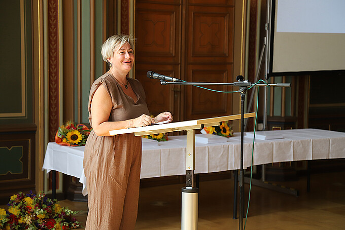 Ute Wunderlich steht am Rednerpult und richtet Glückwünsche an die Absolventinnen und Absolventen.