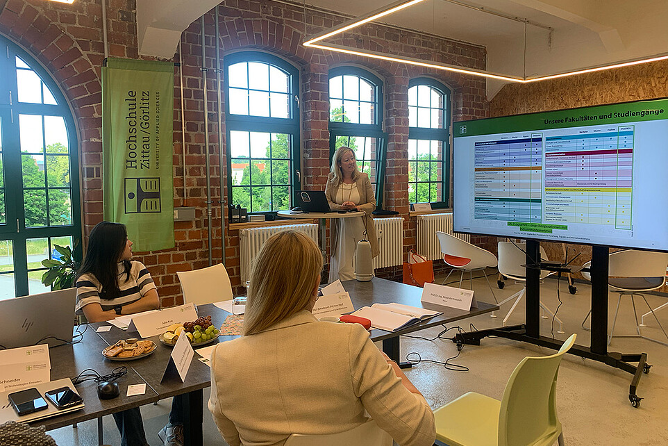 Die Prorektorin hält im Celsiuz vor Gästen einen Vortrag. Neben ihr steht ein Bildschirm und eine HSZG-Flagge.