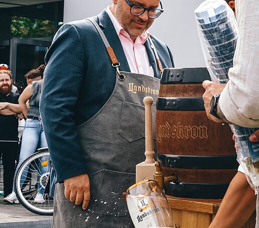 Der Rektor steht bekleidet mit einer Schürze vor einem Bierfass.