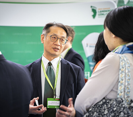 Lian-Ruey Ke im Gespräch mit Teilnehmenden der Konferenz, vor einem grünen Infostand.