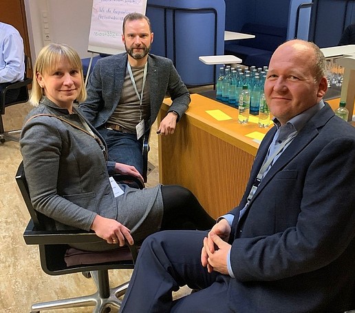 Zwei Männer und eine Frau sitzen in einer Workshop-Situation an einem Tisch