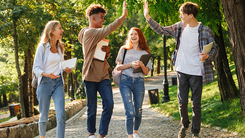 Eine Gruppe Studierender laufen lachend auf einer Allee entlang.