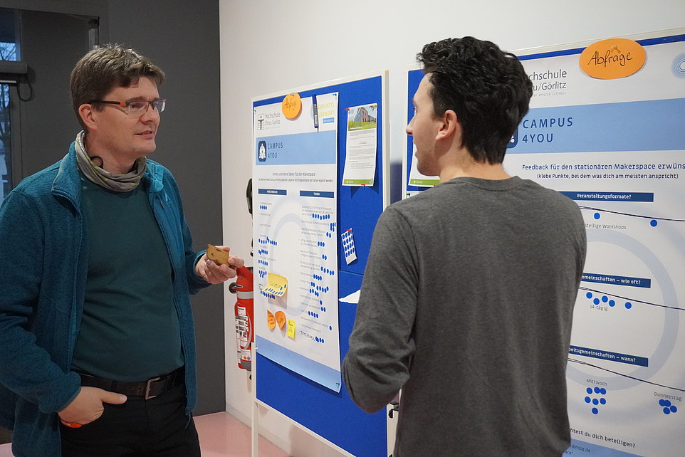 Zwei Teilnehmer stehen vor zwei Postern und unterhalten sich.