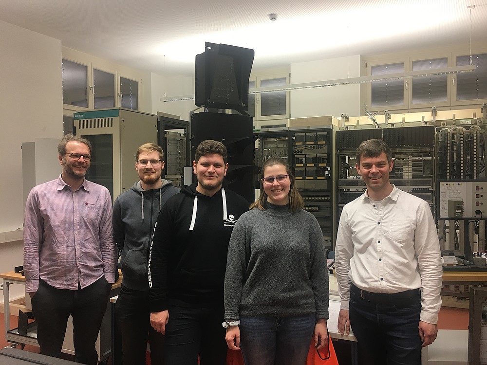 Fünf Personen in einem Labor. Im Hintergrund sieht man aufgebaute Anlagen und Schränke