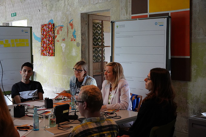 Eine Gruppe von Teilnehmenden sitzt um einen Tisch und diskutiert Ideen in einem Workshop.