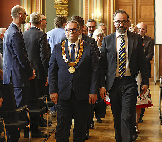 Der Ehrenzug, angeführt vom Rektor und dem Wissenschaftsminister, zieht feierlich aus dem Bürgersaal aus am stehenden Publikum.