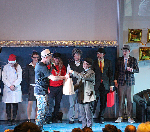 Eine Darstellerin überreicht Herrn Jeschke einen Beutel.