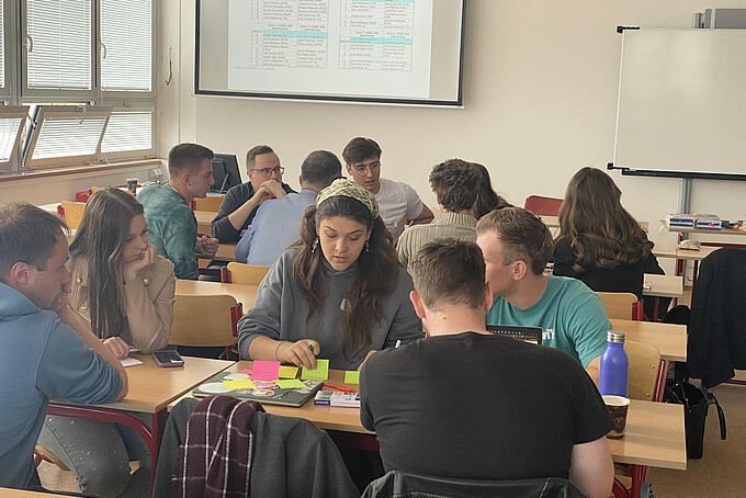 Eine Gruppe von Studierenden sitzt am Tisch und arbeitet etwas aus.