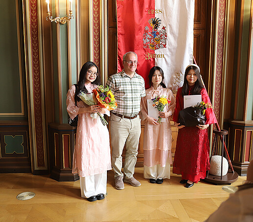 Ein Dozent steht mit einer Gruppe von Absolventinnen vor der Zittauer Fahne zum Gruppenbild.