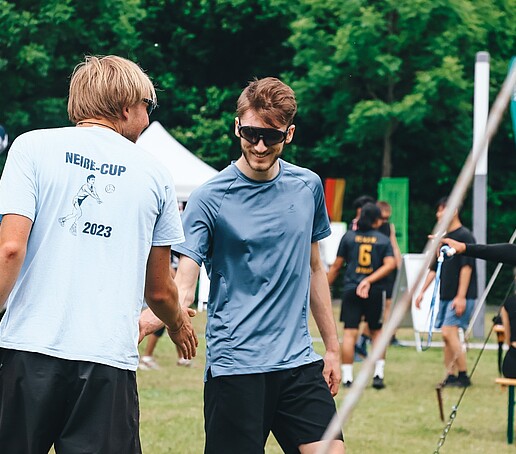 Zwei Sportler reichen sich auf der Wiese die Hand.