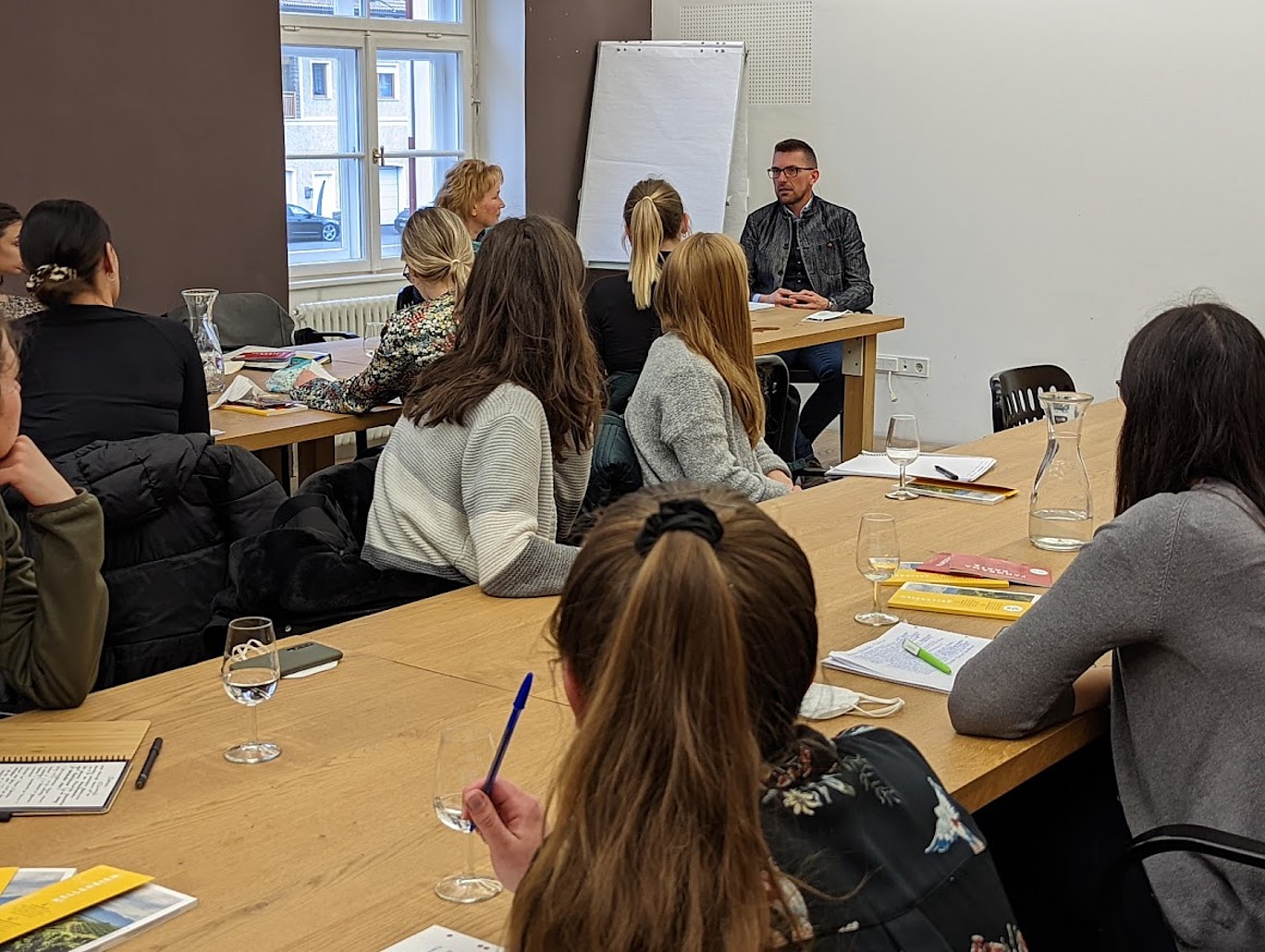 viele Personen an zwei Tischen, mit Schreibutensilien  und Gläsern