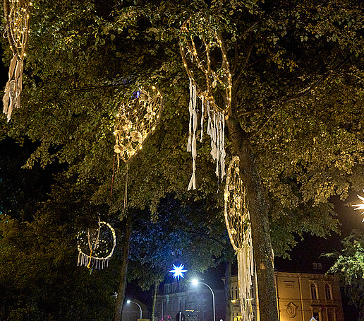 Mit Lichtern bestickte Traumfänger hängen in einem Baum.