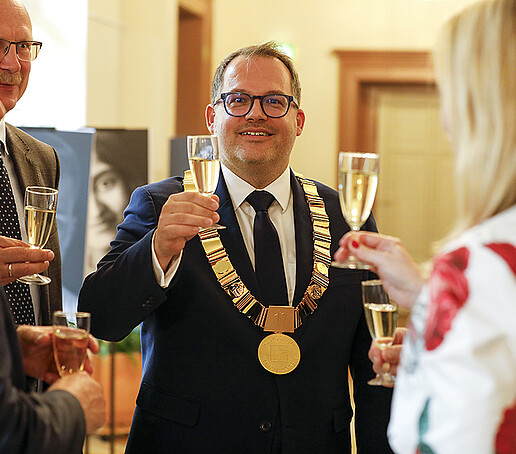 Der Rektor erhebt sein Sektglas umringt von Gästen.