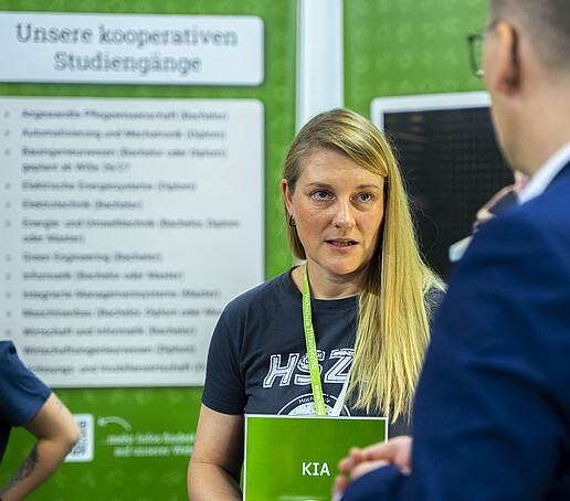 Ein Mann im Anzug unterhält sich mit der KIA-Beauftragten am KIA-Stand.