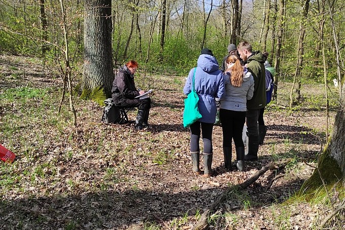 Auf einer Wiese im Wald sitzt Professorin Heidger umringt von Studierenden.
