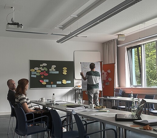 2 Teilnhemer schauen zu einem Referenten am Flipchart