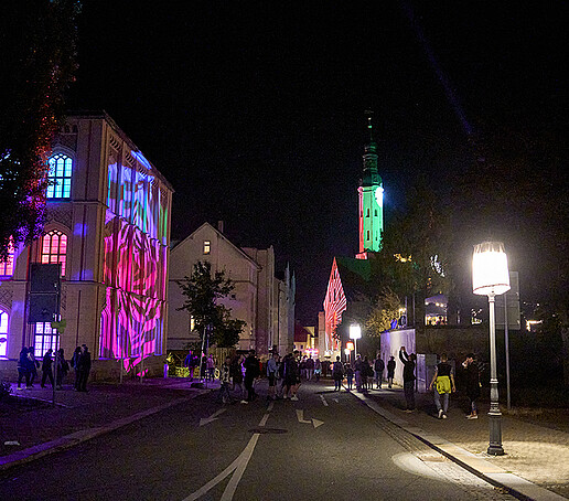 Die Klosterkirche ist hell angeleuchtet im Hintergrund, links davon ist der Heftergiebel lila angeleuchtet.
