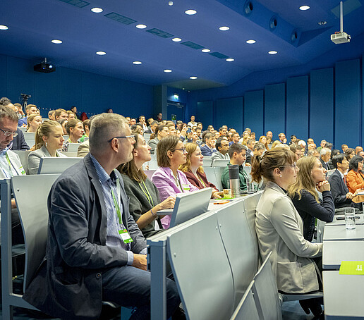Gut gefüllter Hörsaal während eines Vortrags, die Teilnehmenden folgen aufmerksam dem Geschehen.