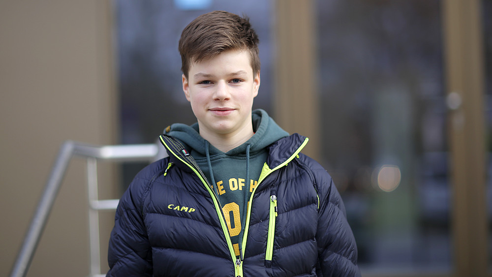 Justus steht vor dem Gebäude Z 1 und lächelt in die Kamera.