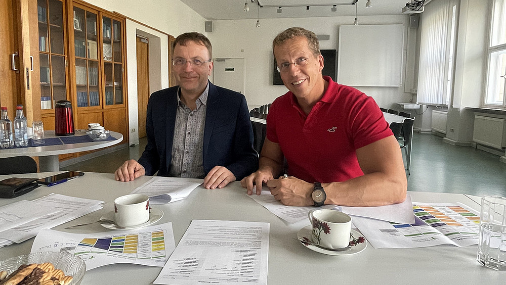 Prof. Jörg Kroschel, Dekan der Fakultät Wirtschaftswissenschaften und Wirtschaftsingenieurwesen der Hochschule Zittau/Görlitz (li.) sowie doc. Ing. Aleš Kocourek, Ph.D., Dekan der Faculty of Economics der Technischen Universität Liberec sitzen am Tisch voller Unterlagen und lächeln in die Kamera.