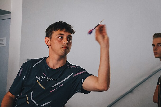 Ein Student hält einen Dartpfeil zum Abschuss in der Hand.