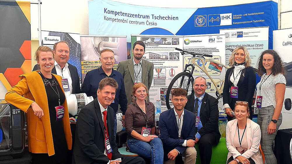 Vertretende von Life and Technology und sächsischen Unternehmen posieren vor einem Messestand des IHK Dresden.