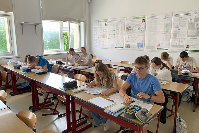 Schülerinnen und Schüler bearbeiten Lernaufgaben an Tischen im Seminarraum.