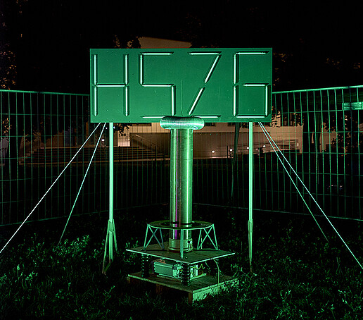 Das HSZG-Logo leuchtet in neongrün durch Leuchtstoffröhren.